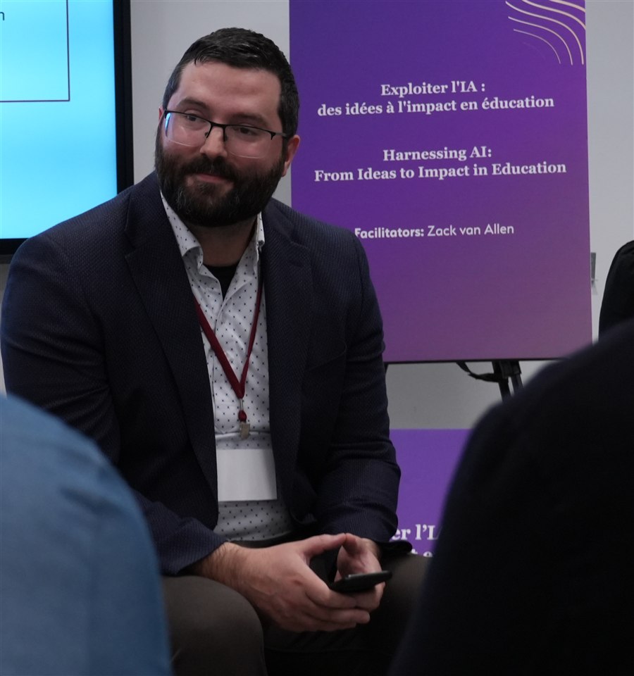 Zack van Allen seated in front of an AI in education workshop display.
